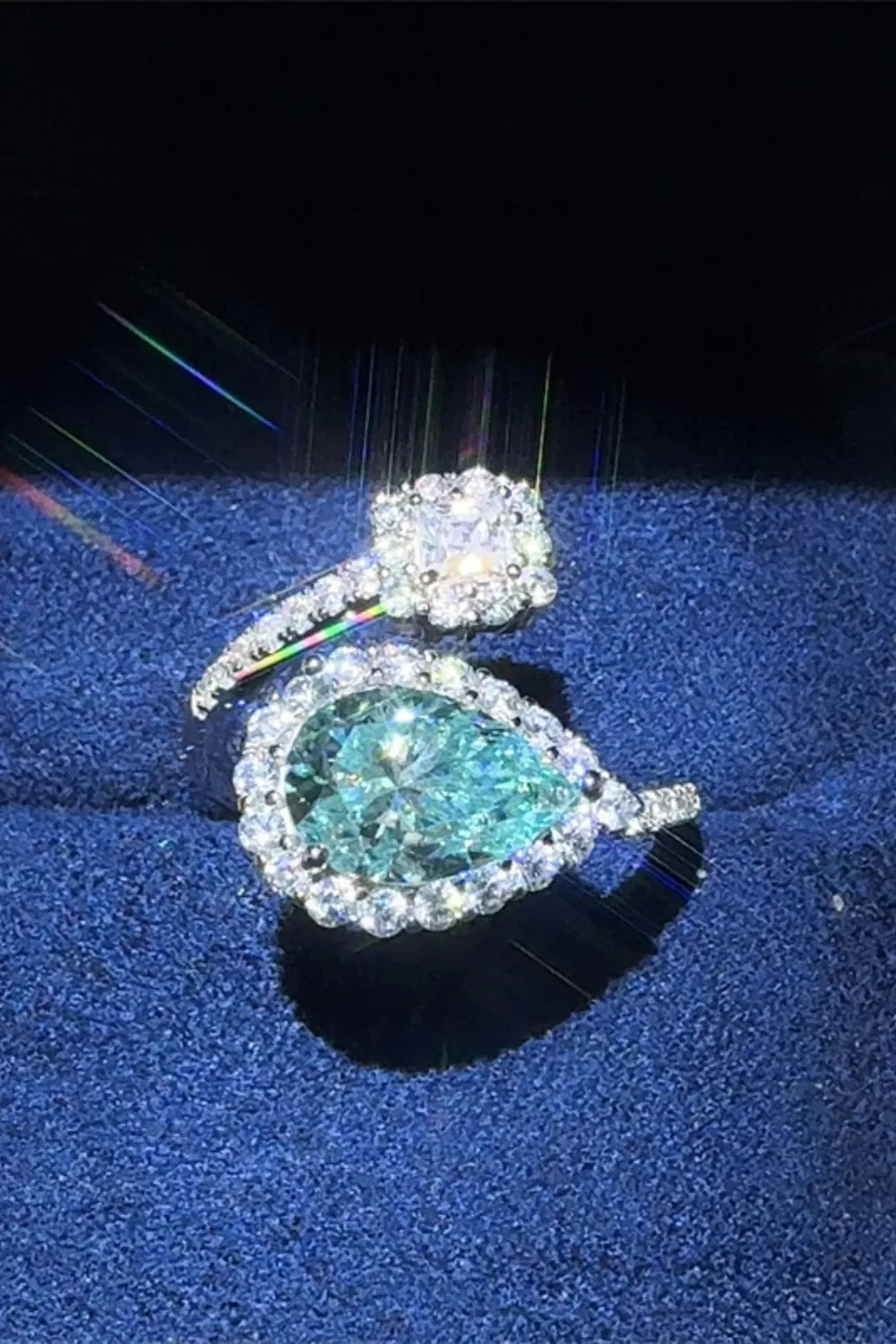 Teardrop-shaped diamond ring with a blue gemstone on a blue cushion against a black background