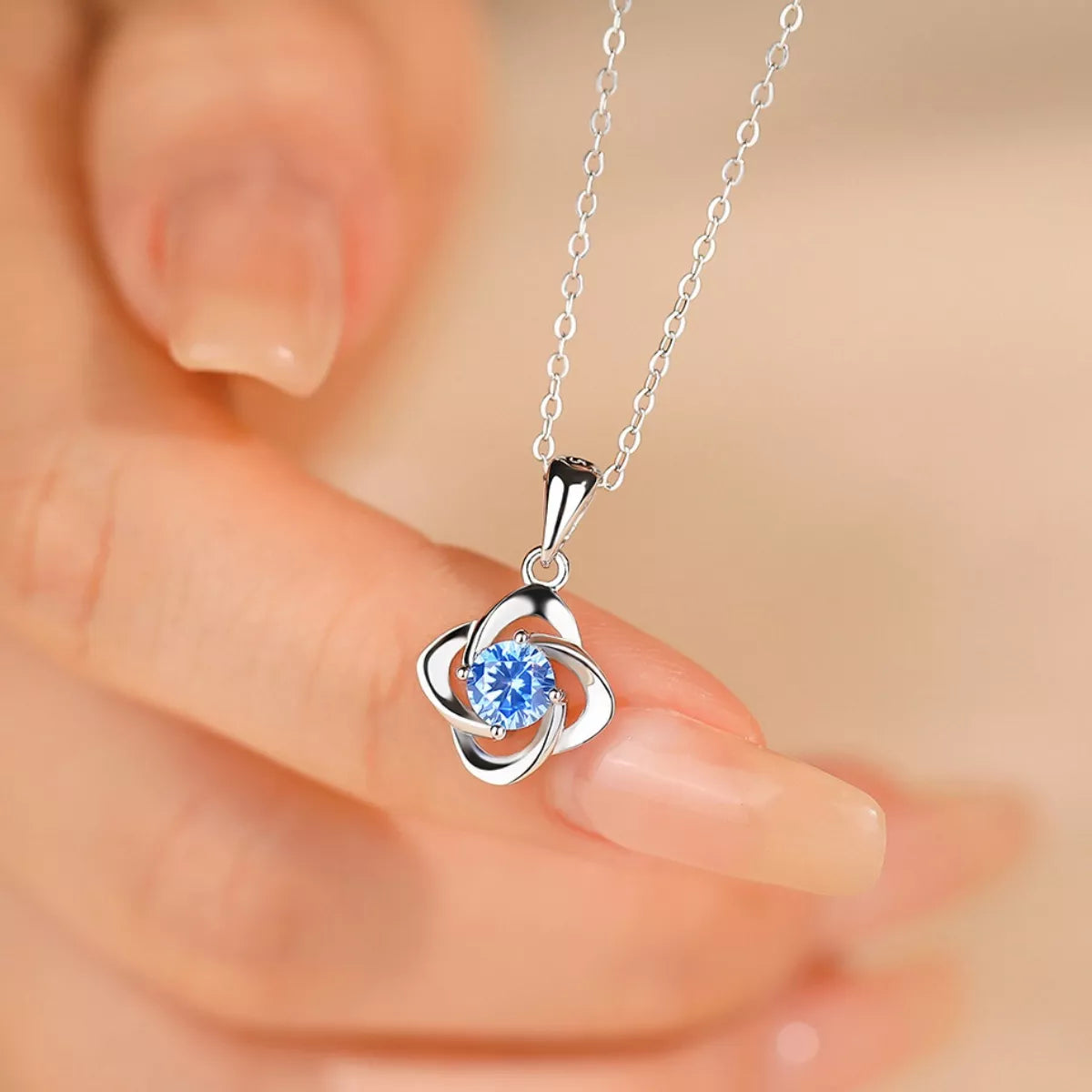 Silver necklace with a blue pendant held by a hand against a blurred background
