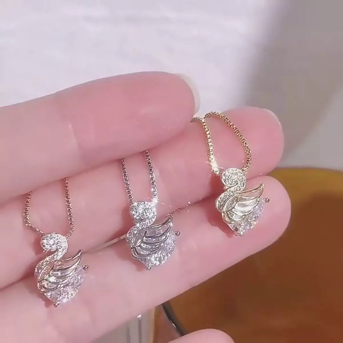 Three delicate necklaces with Swan pendants held in a hand against a blurred background