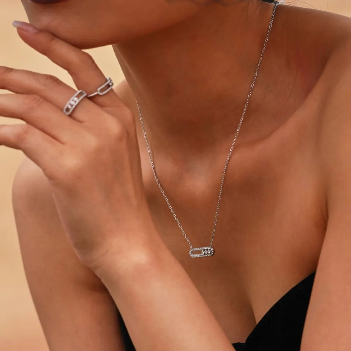 Close-up of a person wearing a silver necklace with a rectangular pendant on a beige background