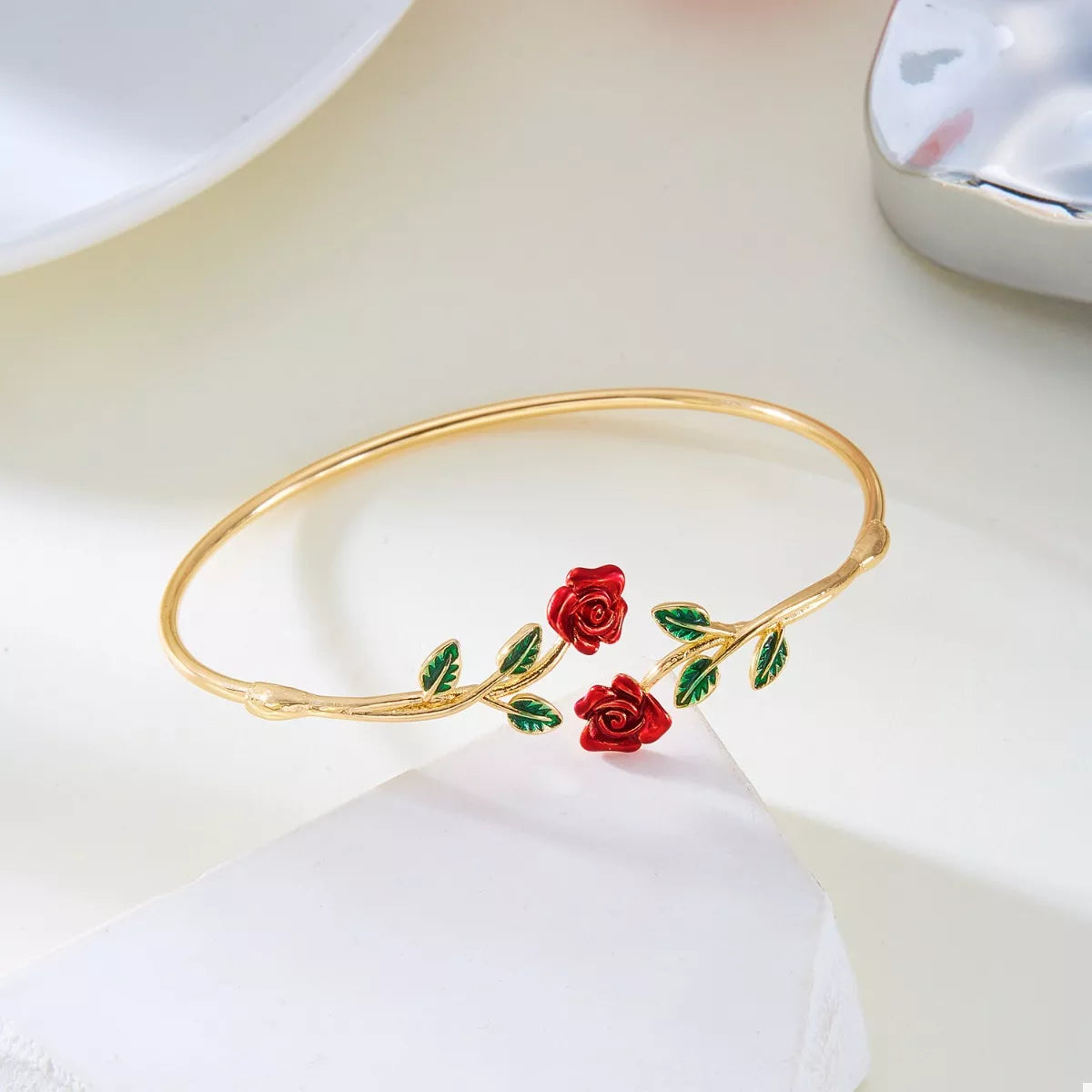 Gold bracelet with red rose designs on a white surface