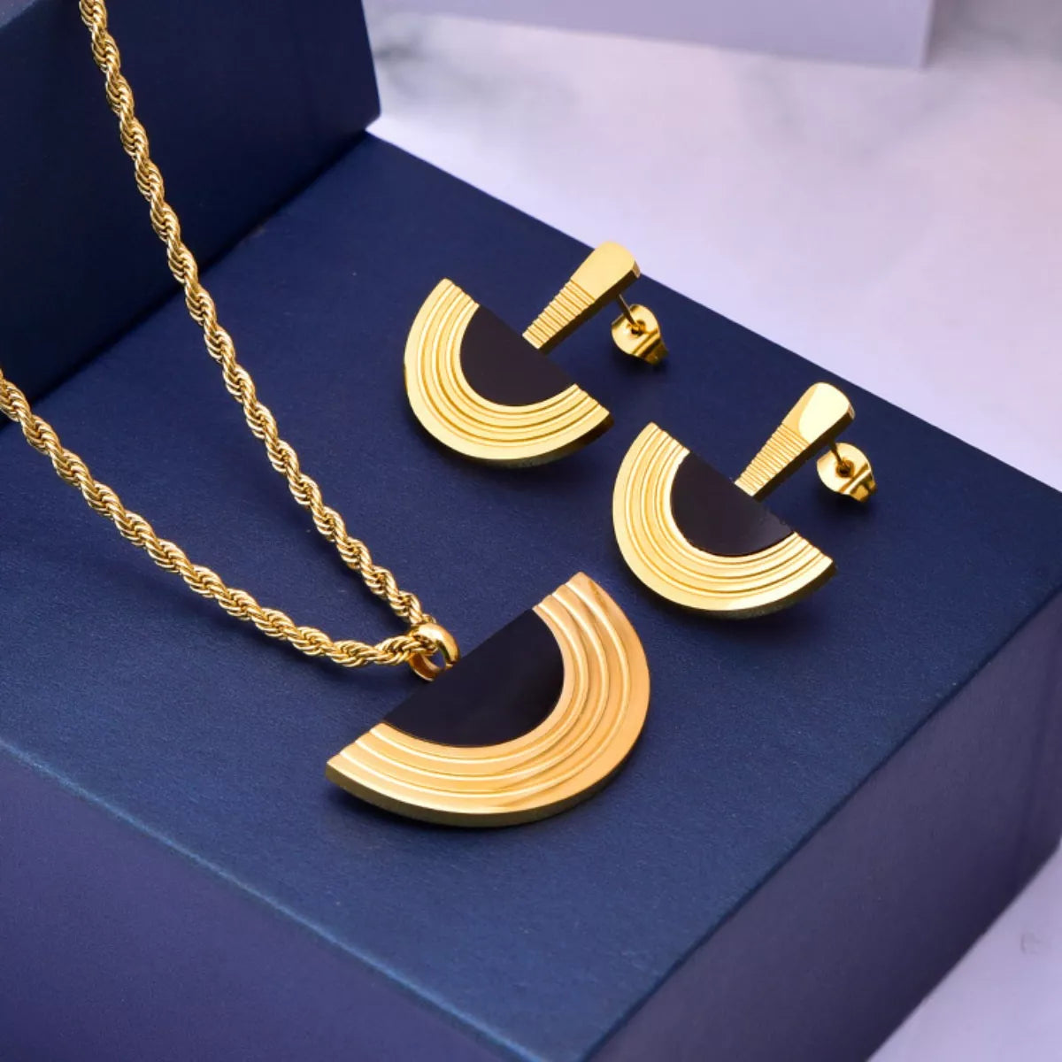 Gold necklace and earrings set on a blue box
