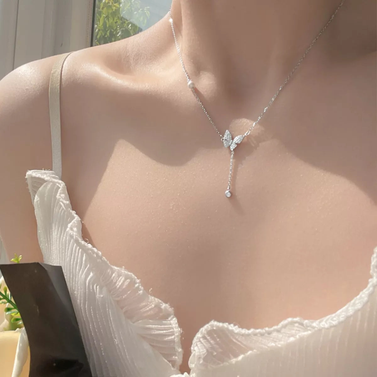 Silver butterfly necklace on a model wearing a white top.