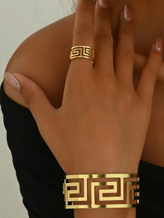Gold bracelet and ring on a hand against a neutral background
