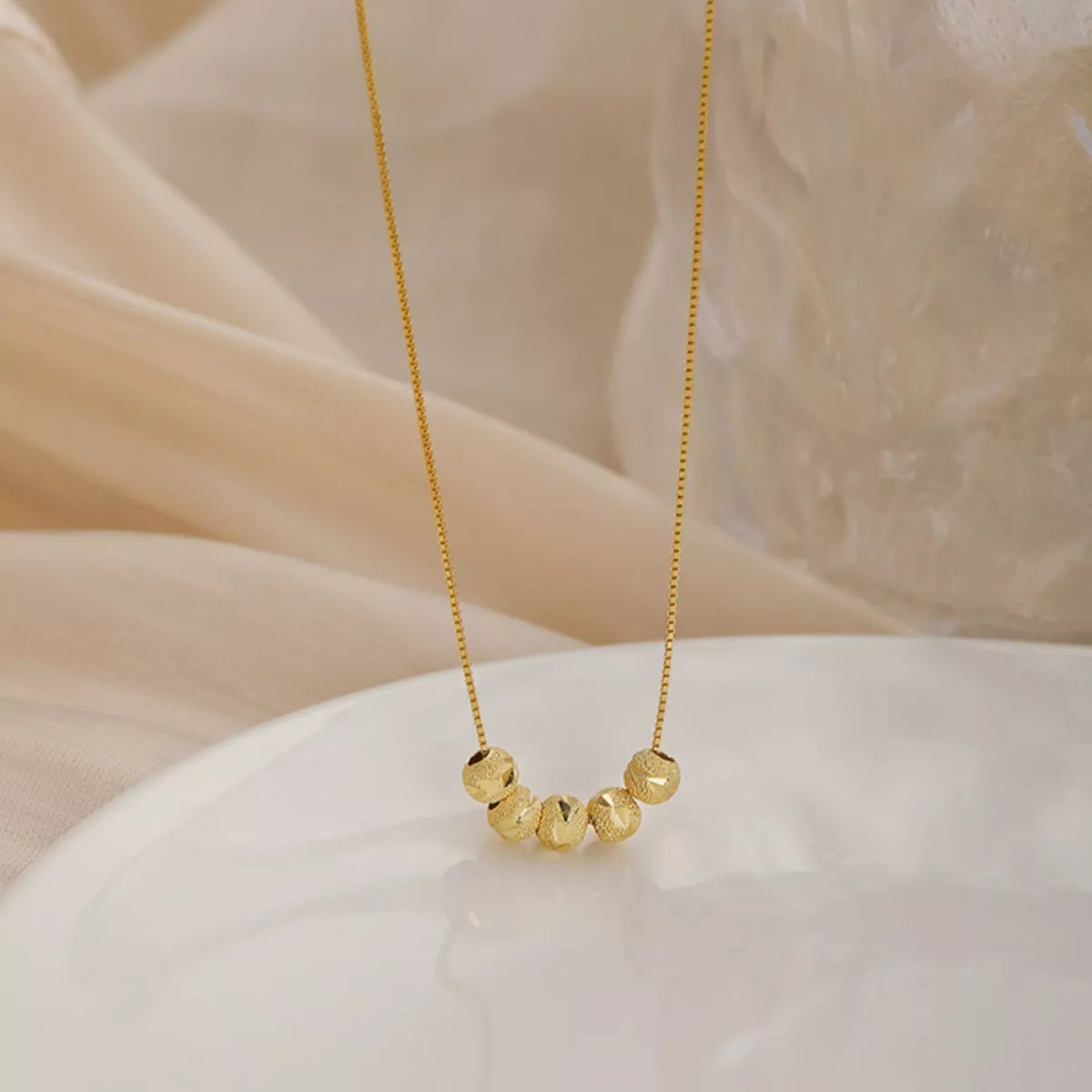Gold necklace with beaded pendant on a soft beige fabric background