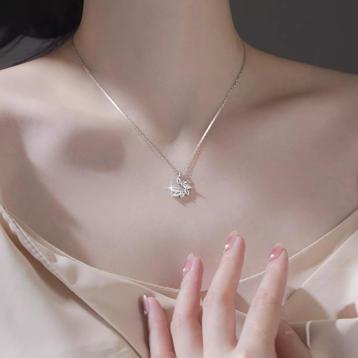 Necklace with a delicate pendant worn by a person, with a hand touching the neckline.