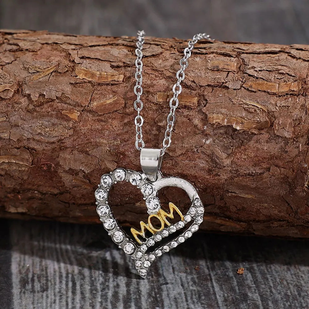 Heart-shaped pendant with 'MOM' on a chain, lying on a wooden surface.