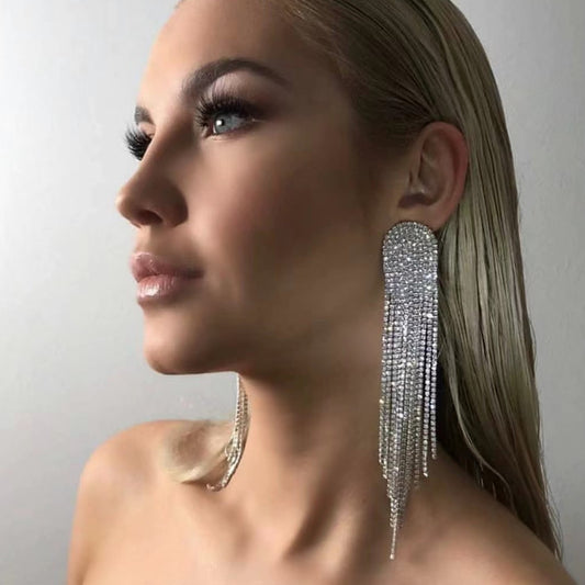 Woman wearing sparkling tassel earrings against a neutral background