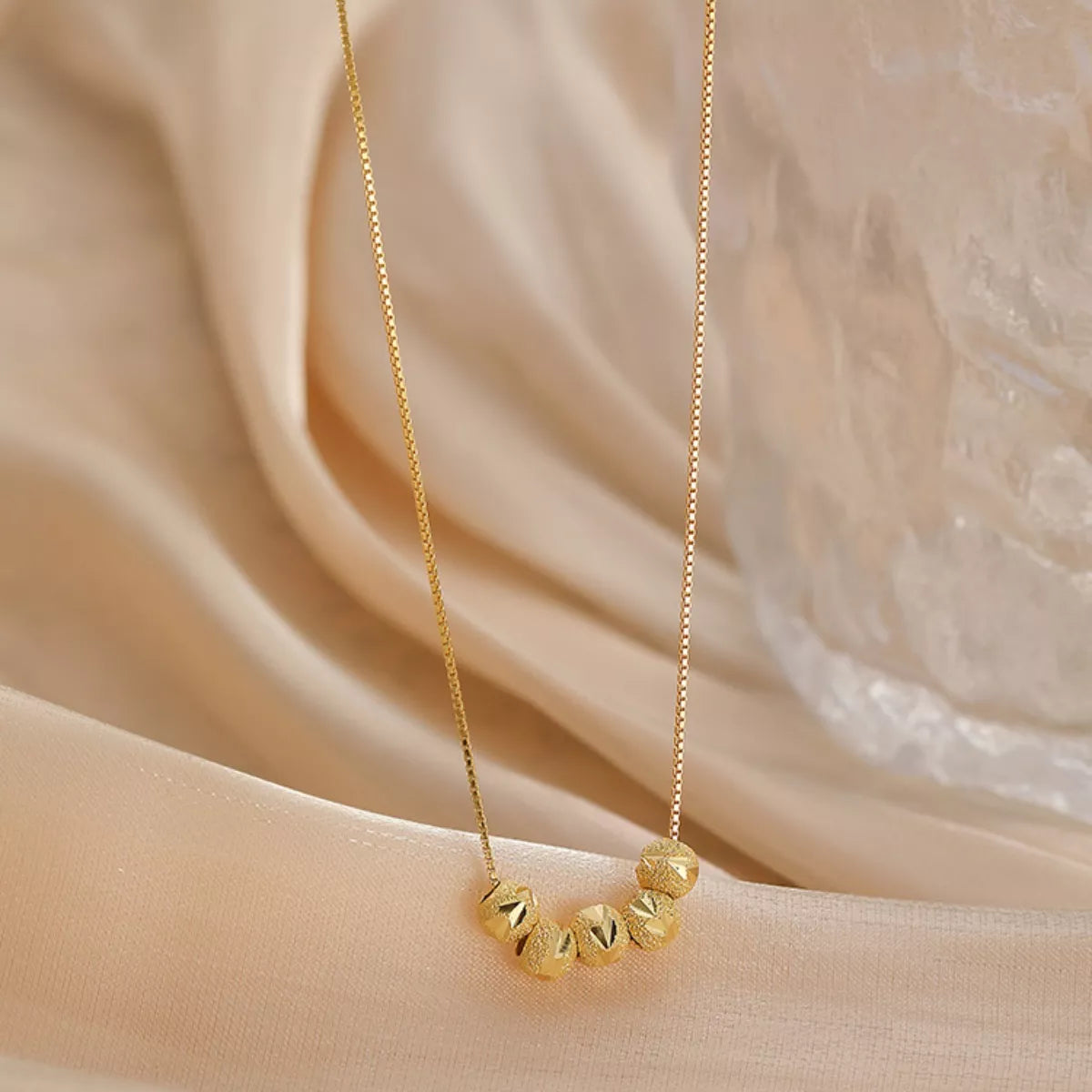 Gold necklace with small beads on a beige fabric background