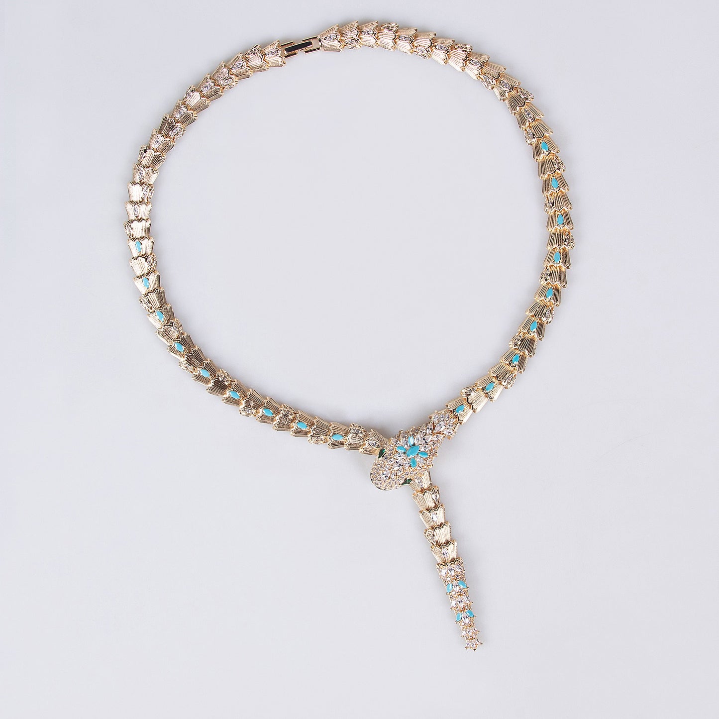 Gold snake necklace with turquoise blue and clear stones on a light background.
