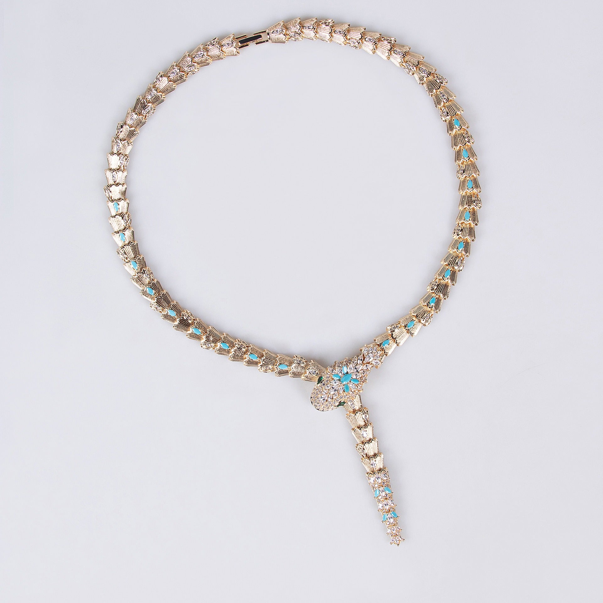 Gold snake necklace with turquoise blue and clear stones on a light background.