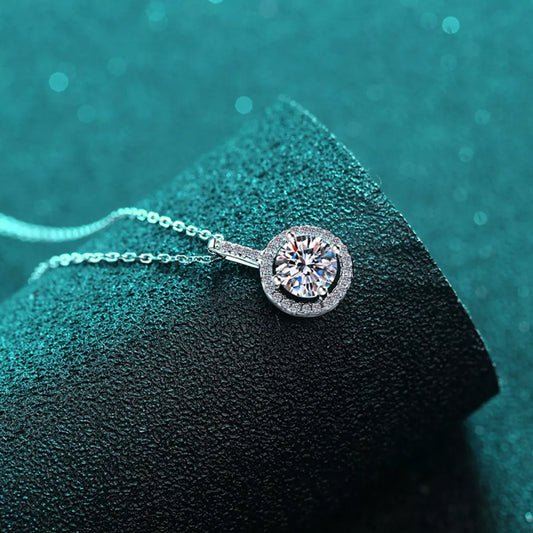 Silver necklace with a round diamond pendant on a textured green surface