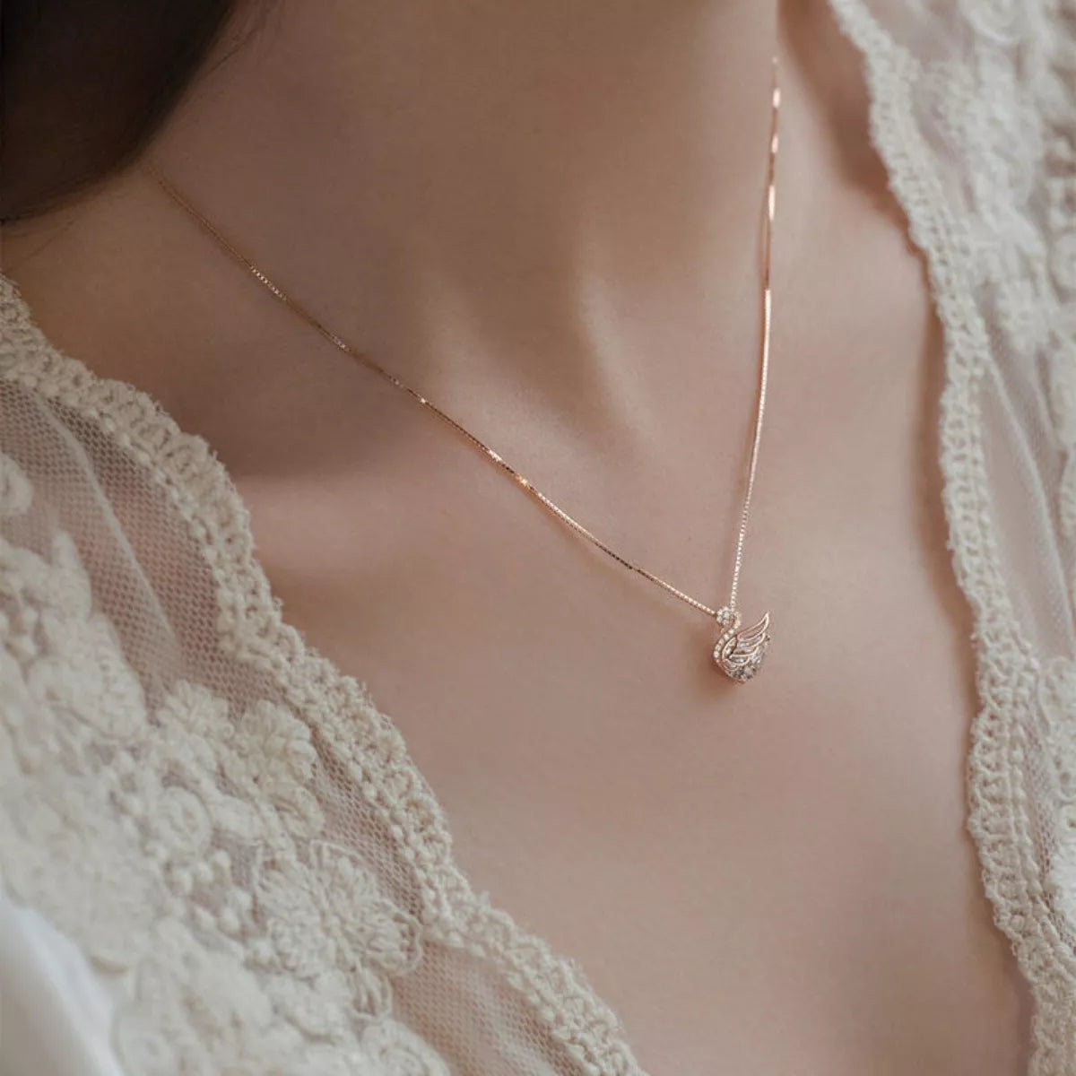 Delicate gold necklace with a heart pendant on a person wearing a lace garment.