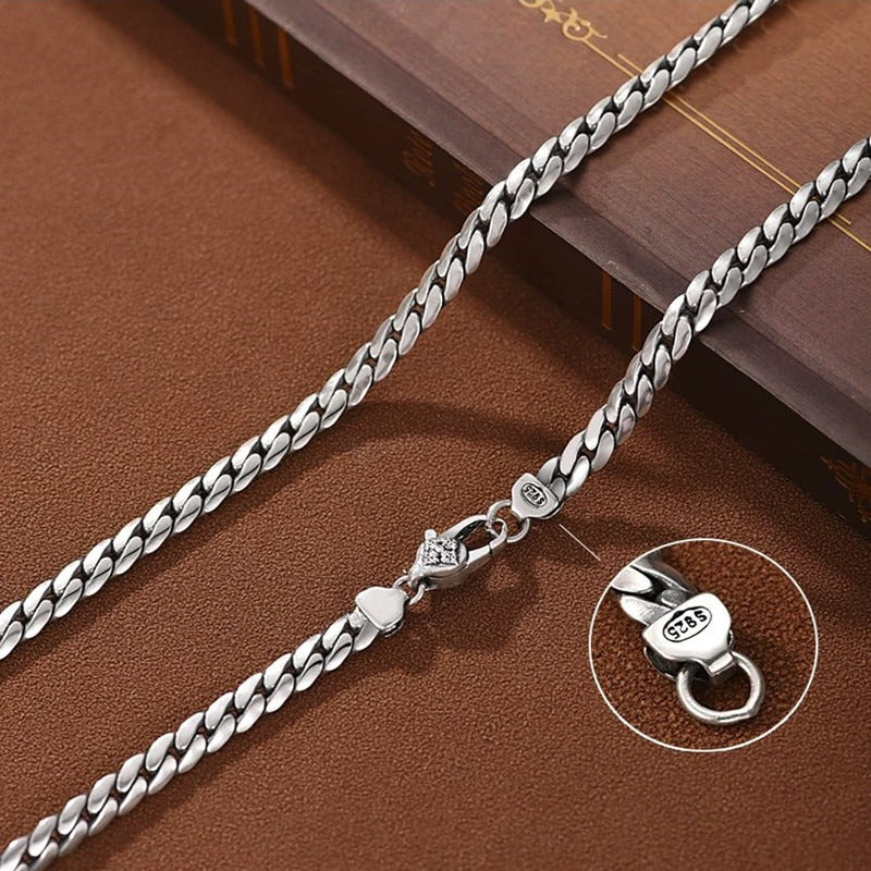 Silver chain necklace on a brown surface with close-up of clasp.