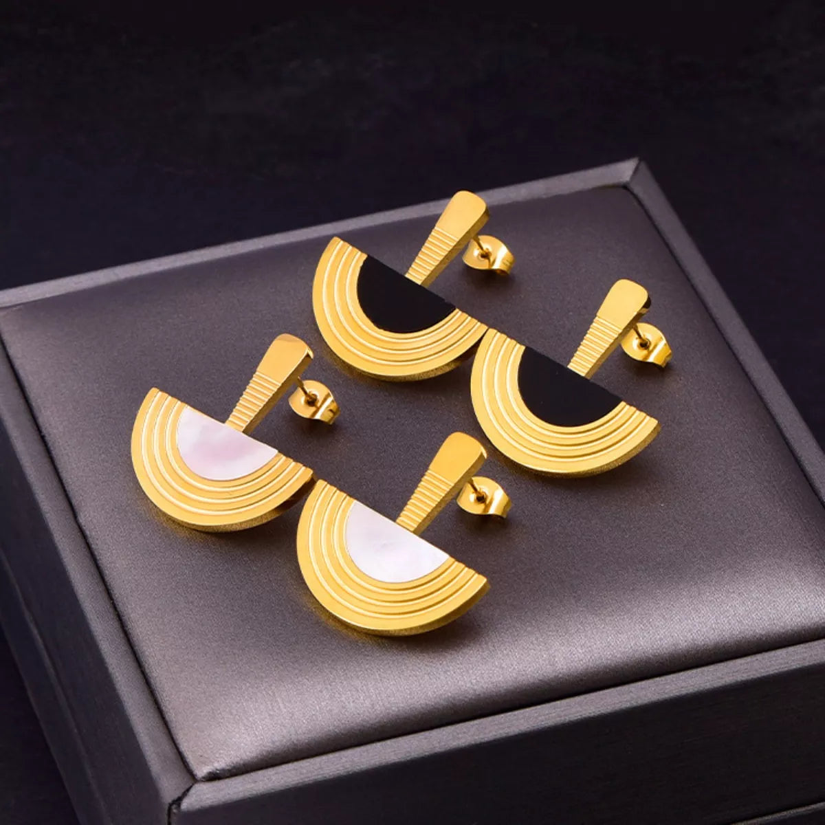 Gold and black geometric earrings on a dark gray box