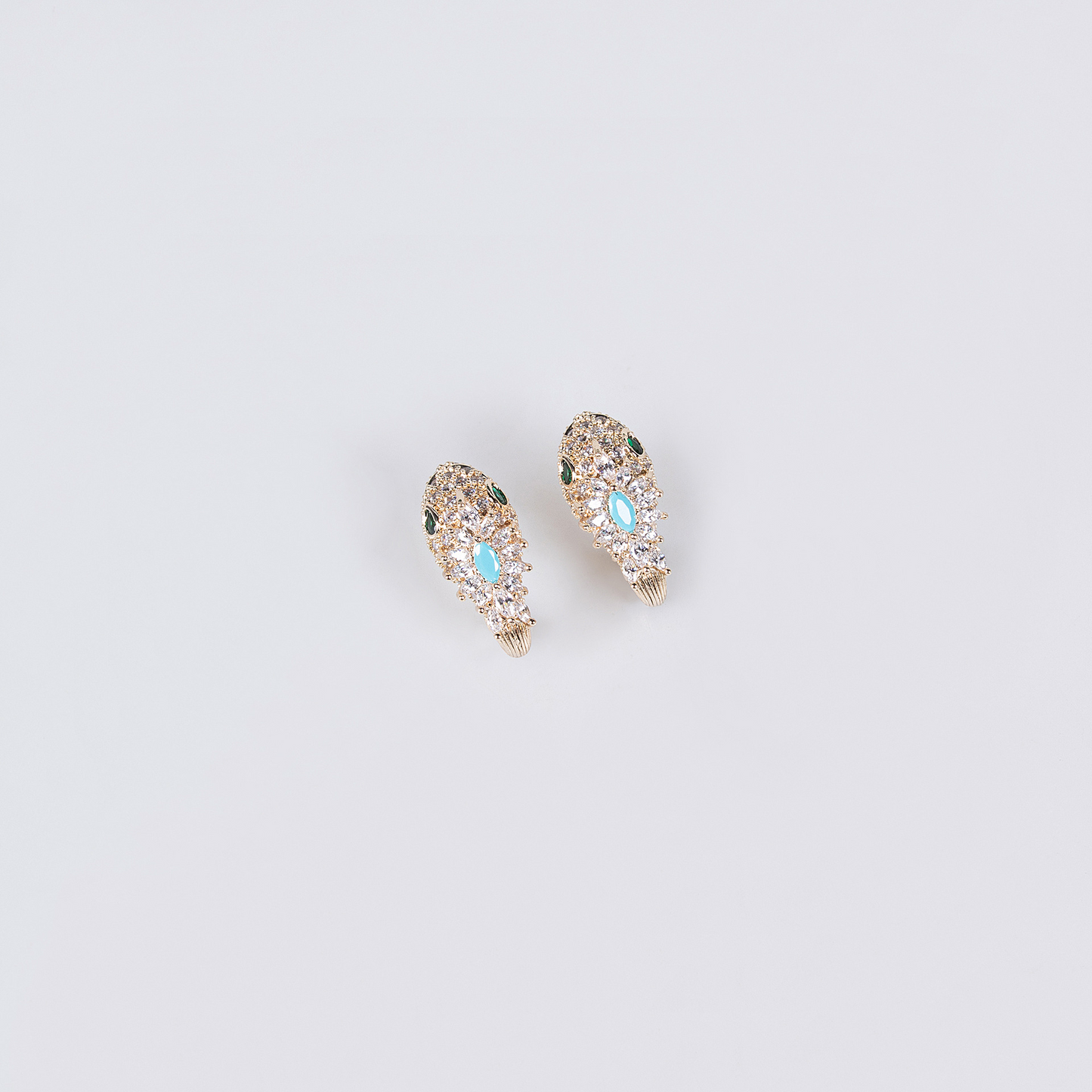Gold snake earrings with turquoise blue and clear stones on a light background.