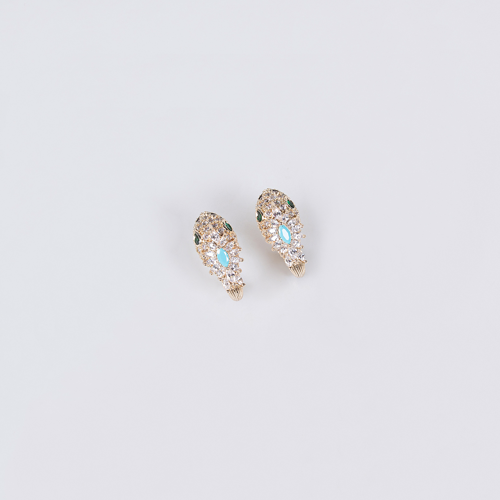 Gold snake earrings with turquoise blue and clear stones on a light background.