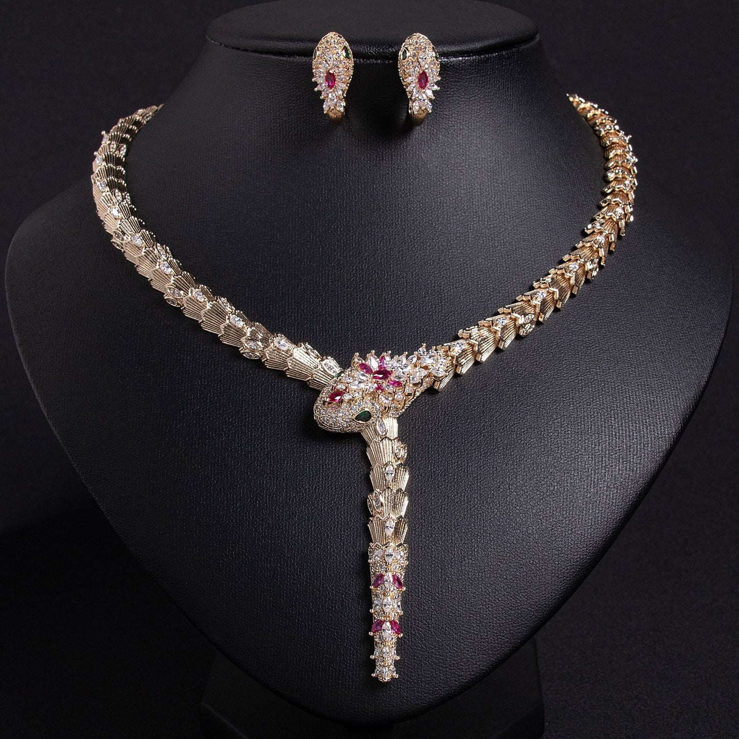 Gold snake necklace and earrings set with red and clear stones, on a black bust.