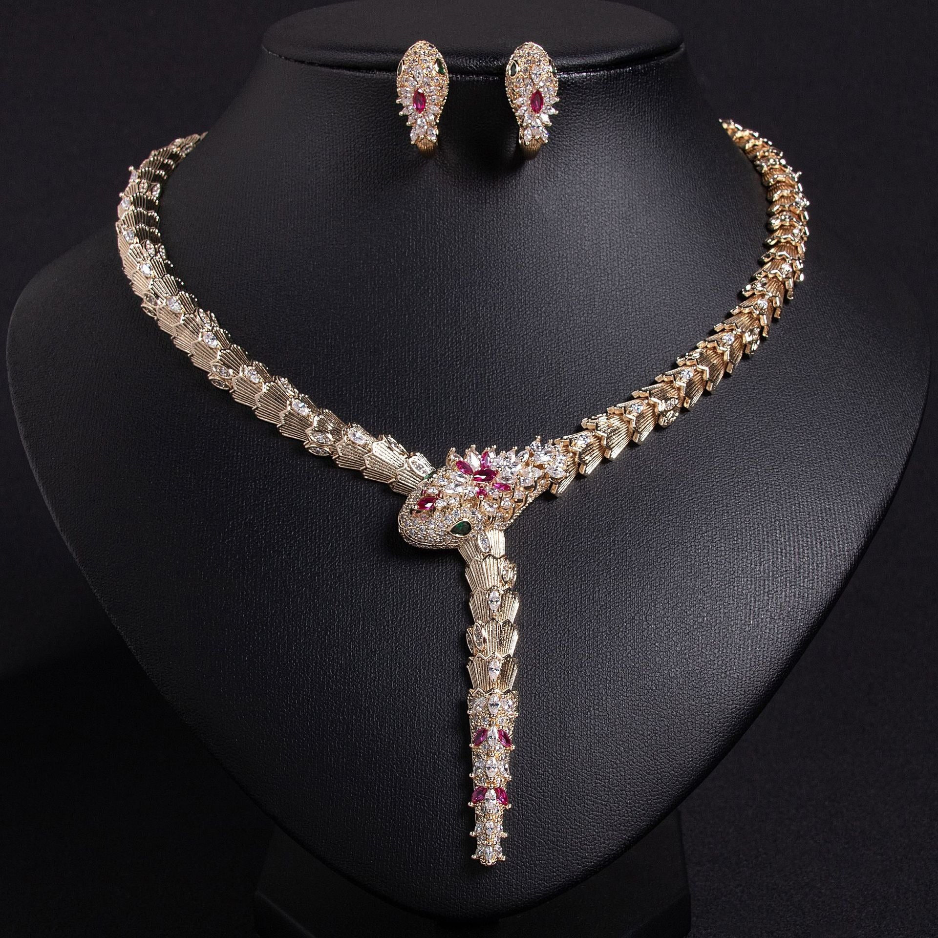 Gold snake necklace and earrings set with red and clear stones, on a black bust.