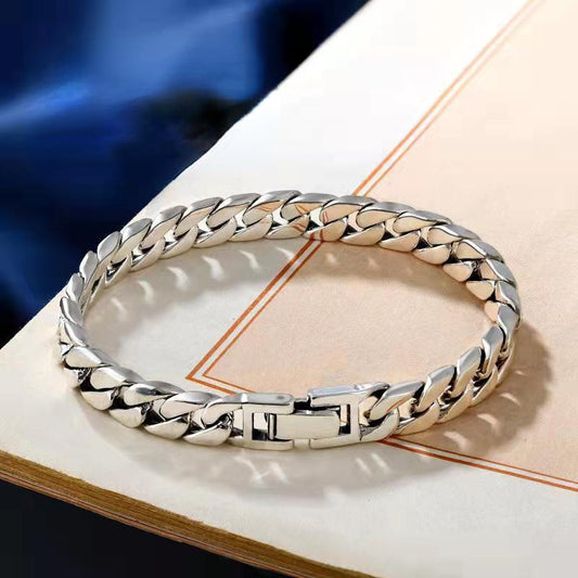 A silver-toned metal chain bracelet with a curb-style link design, resting on an open book with a beige page and dark blue background visible.