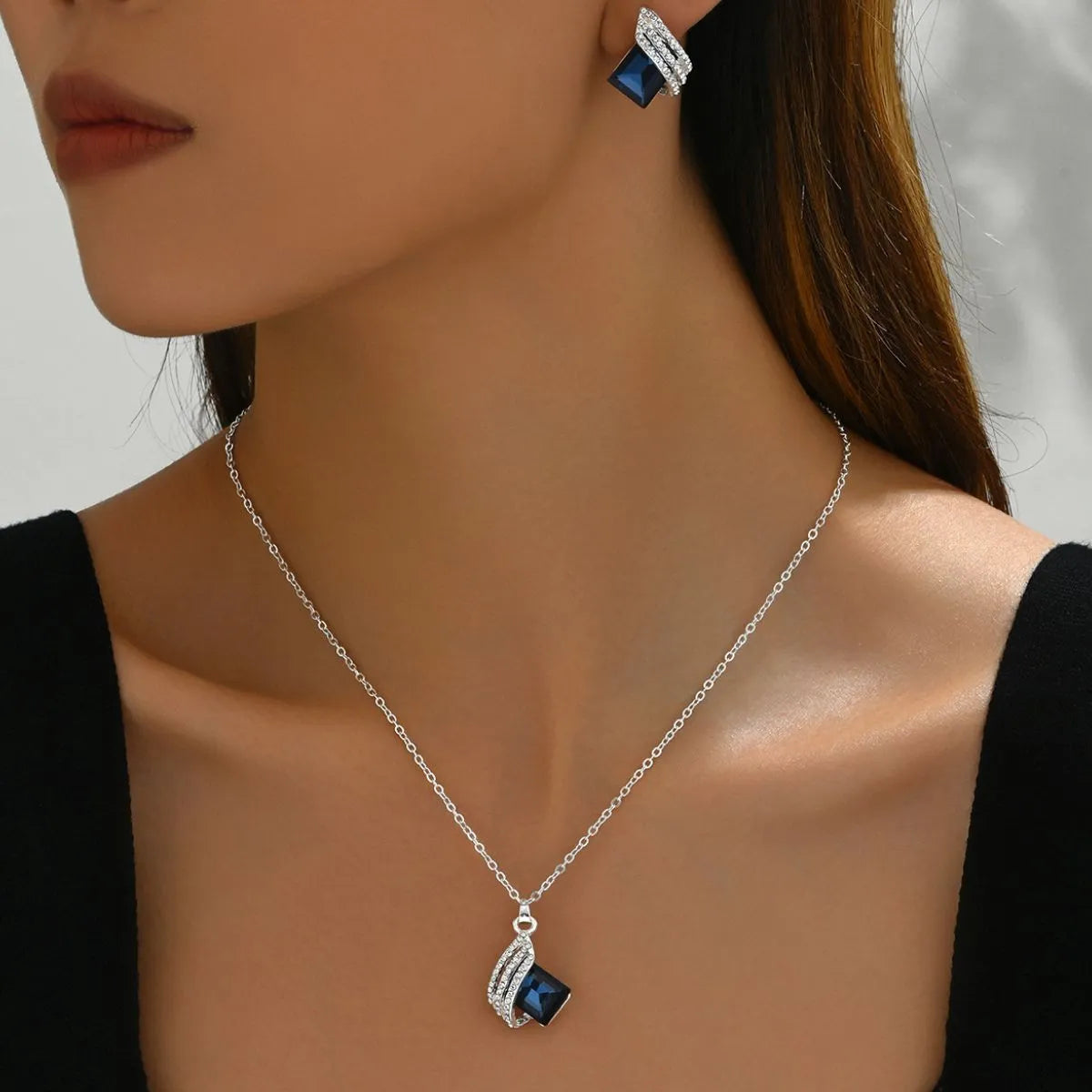 Close-up of a woman wearing a silver necklace with a blue pendant and matching earrings.