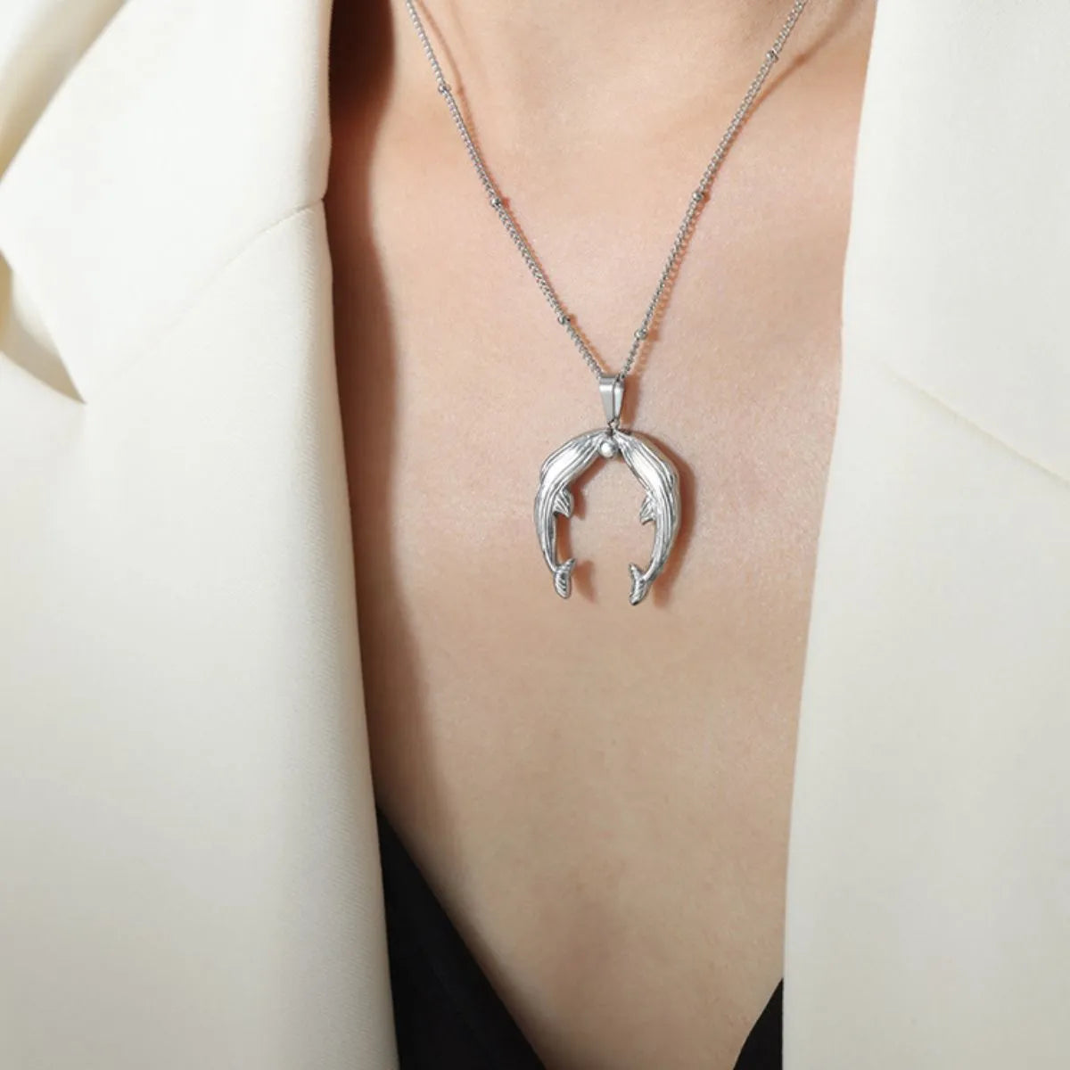 Silver horseshoe pendant necklace on a person wearing a white blazer.