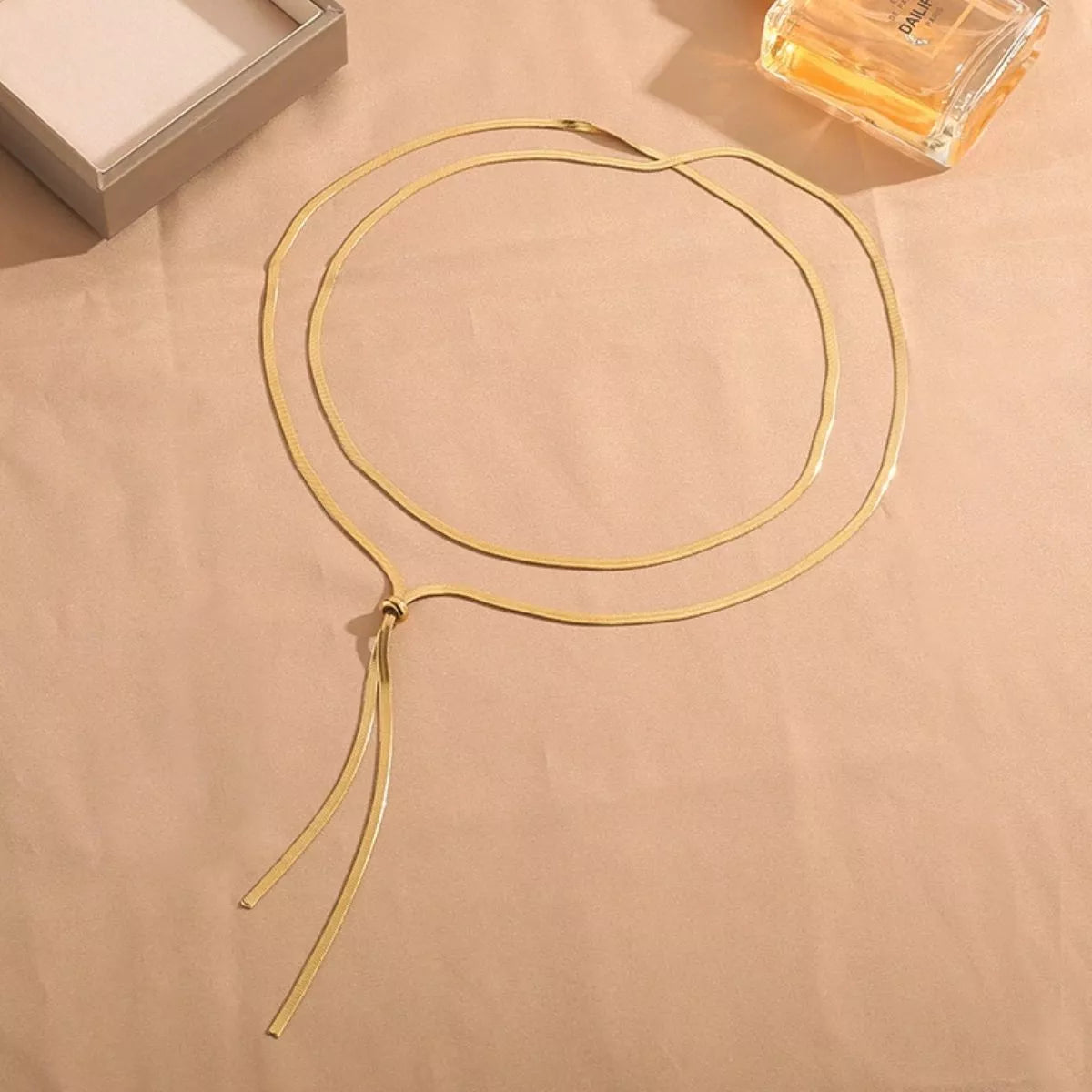 Gold necklace on a beige surface with a box and perfume bottle in the background
