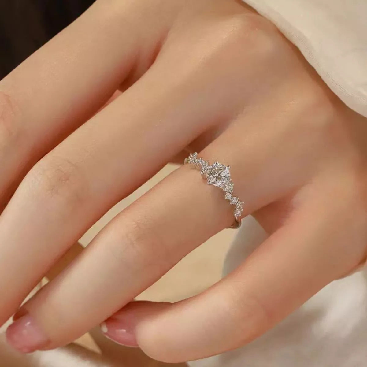 Silver ring with diamonds on a person's finger against a neutral background
