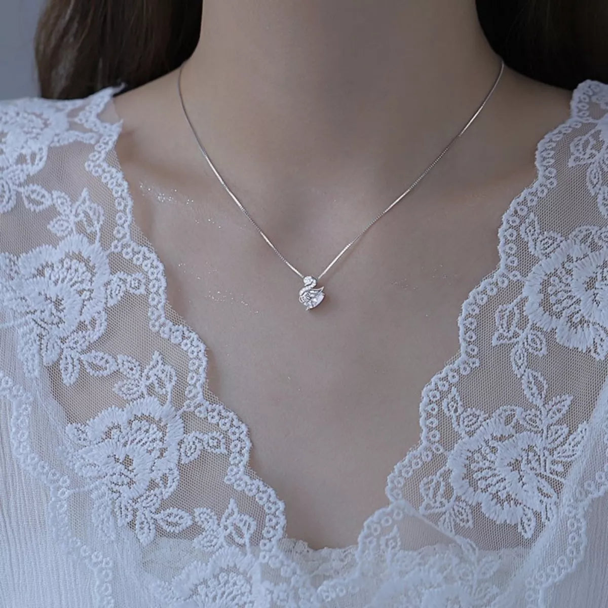 Silver necklace with a heart pendant on a person wearing a lace garment.