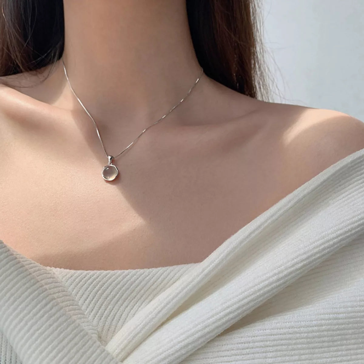 Necklace with a pendant worn by a person in a white outfit