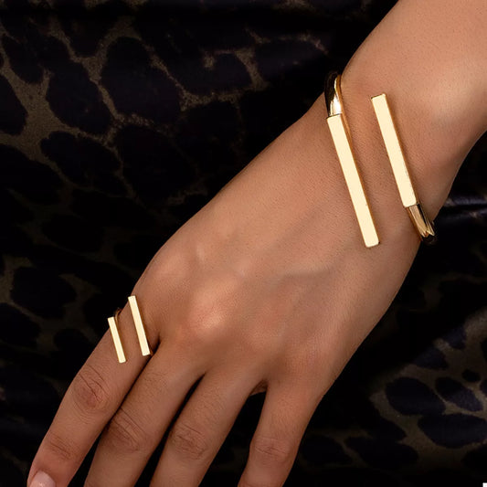 Gold bracelet and ring on a hand against a dark background