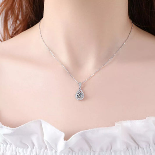 A silver teardrop pendant necklace with a halo setting, worn on a model's neck over a white ruffled top.