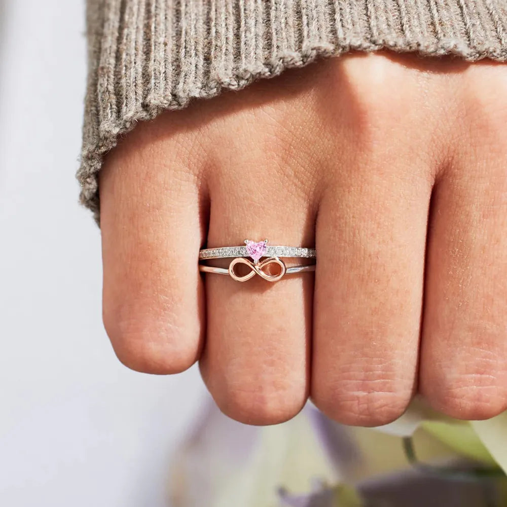 Close-up of a hand wearing two rings with a pink gemstone on a neutral background
