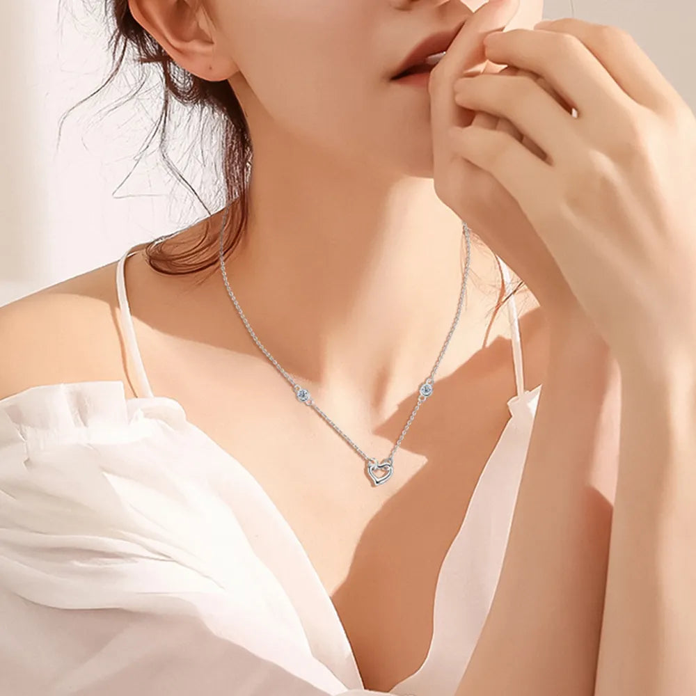 Woman wearing a delicate necklace with a heart-shaped pendant, set against a soft background.