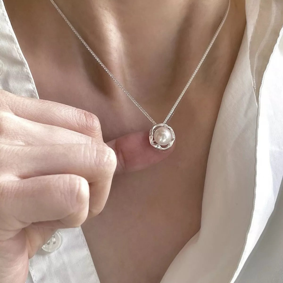 Pearl necklace being worn with a hand adjusting it against a neutral background