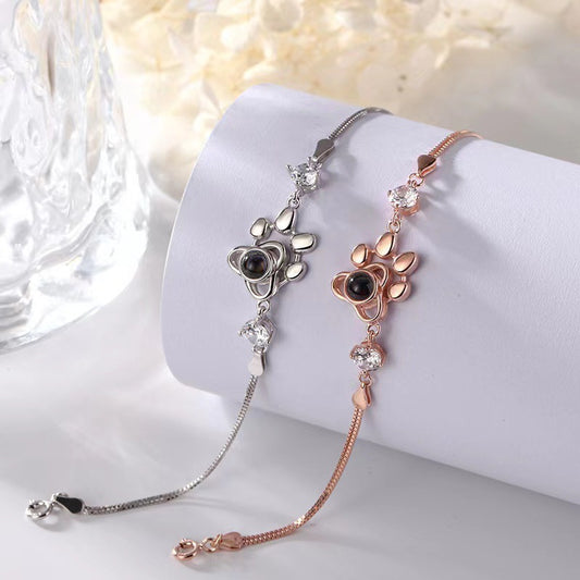 Two floral-themed bracelets, one silver and one rose gold, on a white surface with a blurred background.