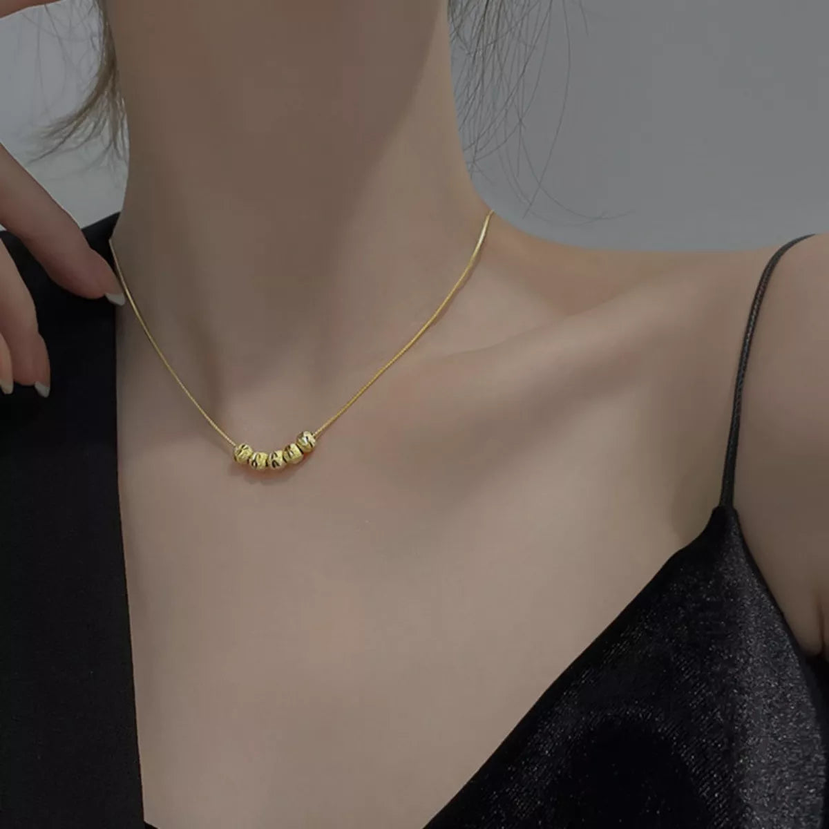 Gold necklace being worn on a person's neck with a neutral background