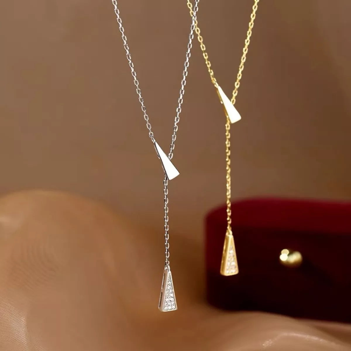 Two necklaces, one silver and one gold, with triangular pendants on a beige surface.