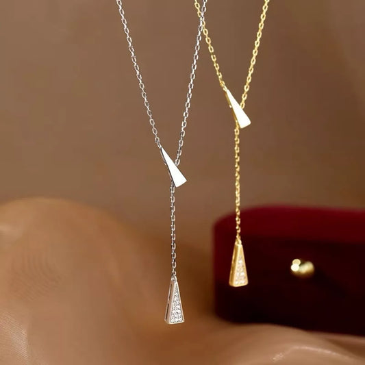 Two necklaces, one silver and one gold, with triangular pendants on a beige surface.