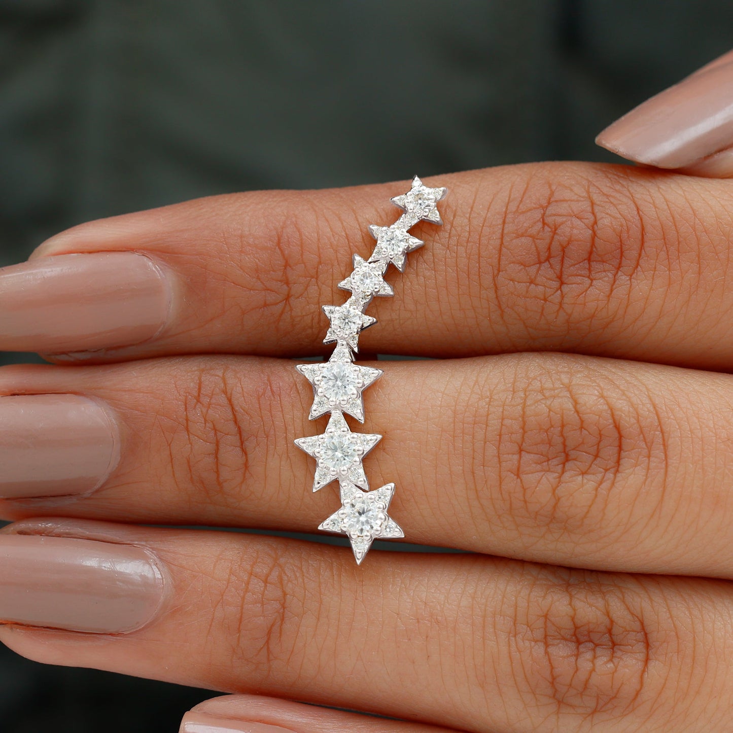 Silver star-shaped earring on a hand against a dark background