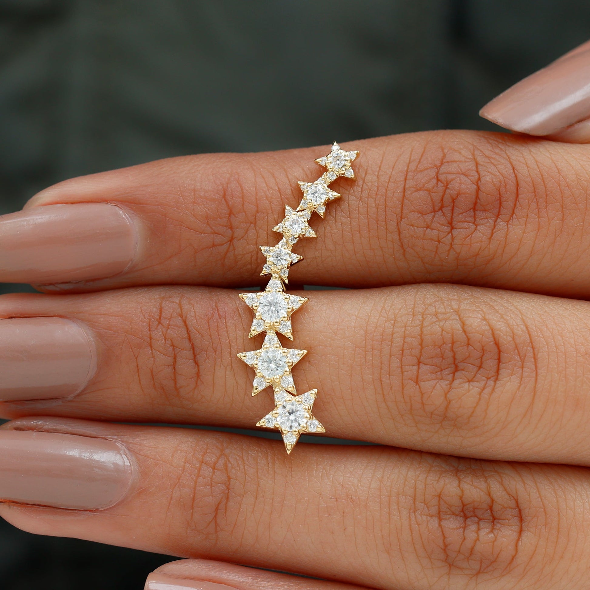 Gold star-shaped earrings on a hand with a blurred background