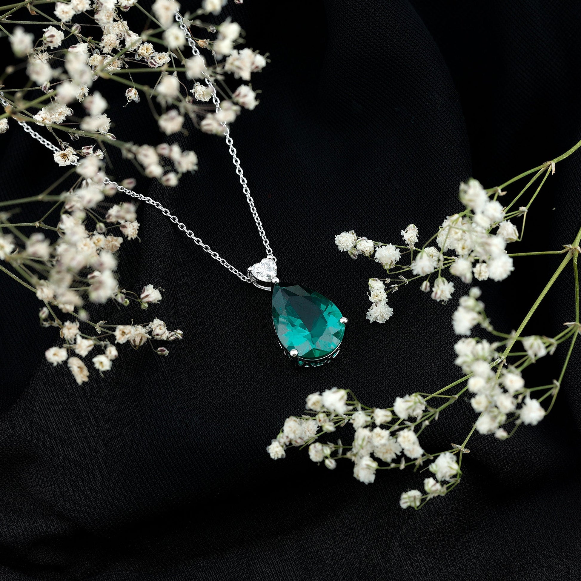 Teardrop-shaped green gemstone necklace on a chain with white flowers against a black background