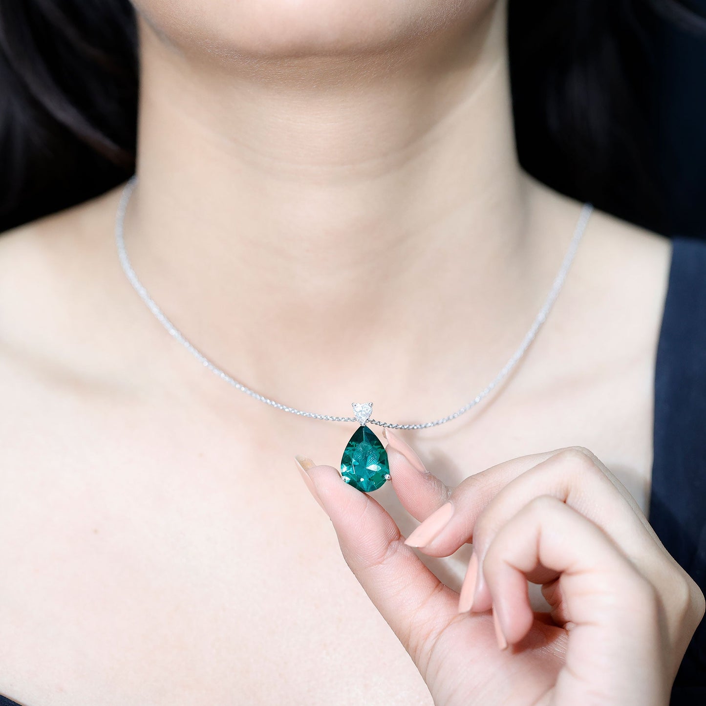 Necklace with a green teardrop pendant held by a hand against a neutral background