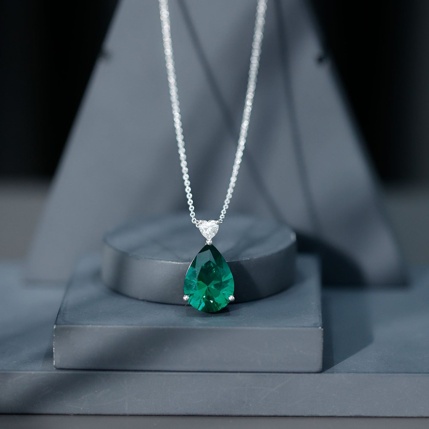 Green emerald pendant necklace on a dark gray stand with a blurred background