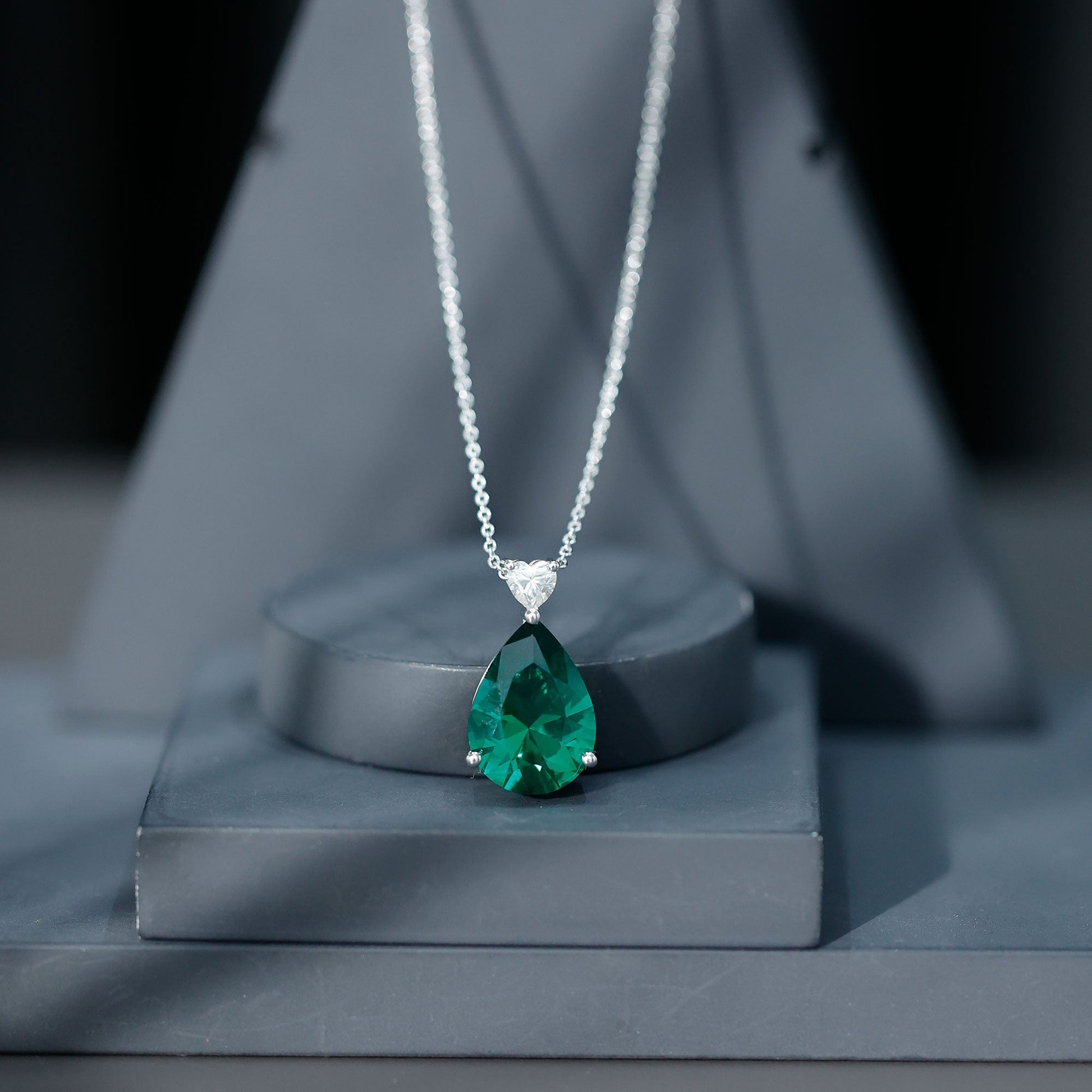 Green emerald pendant necklace on a dark gray stand with a blurred background