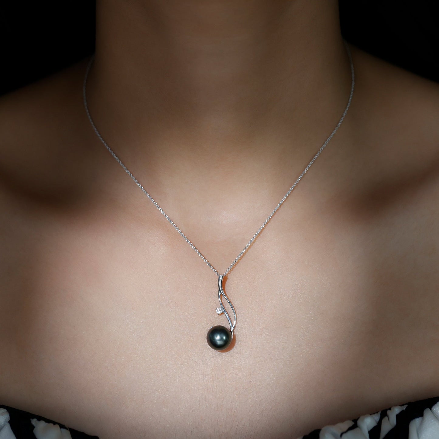Necklace with a black pearl pendant on a person's neck against a dark background