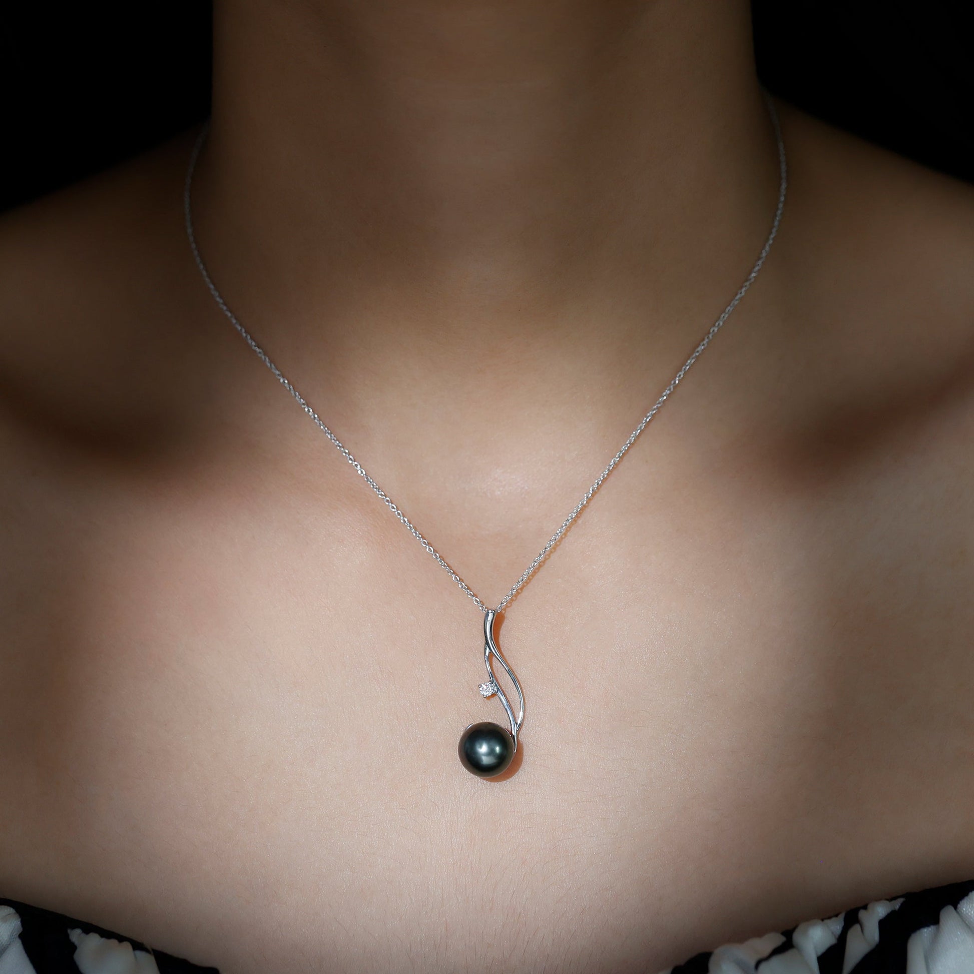 Necklace with a black pearl pendant on a person's neck against a dark background