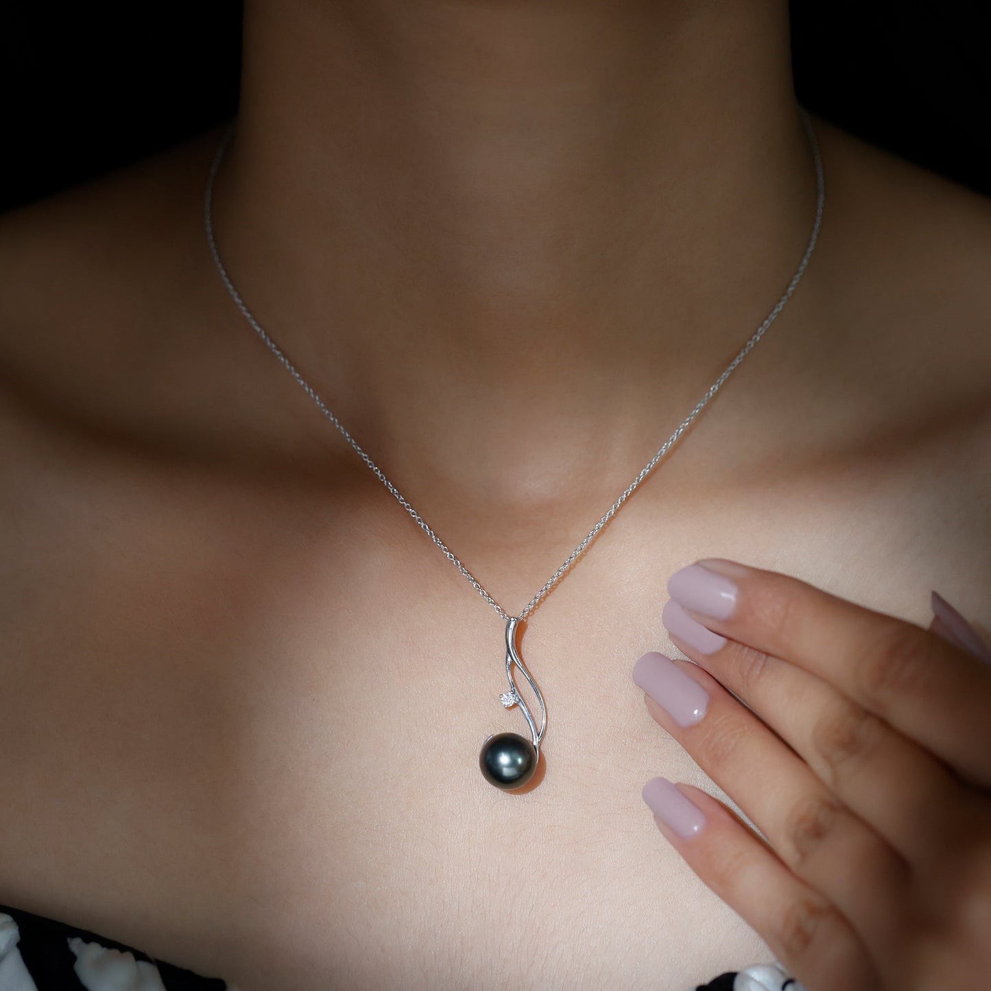 Necklace with a black pendant worn by a person, with a hand touching the necklace.