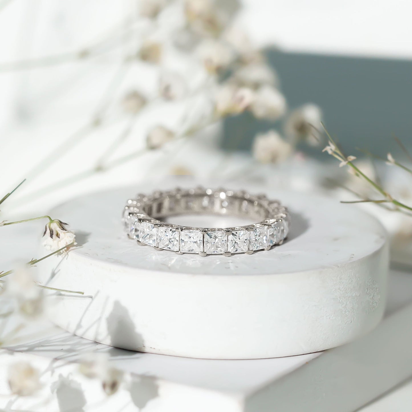 Silver ring with diamonds on a white stone surface with flowers in the background