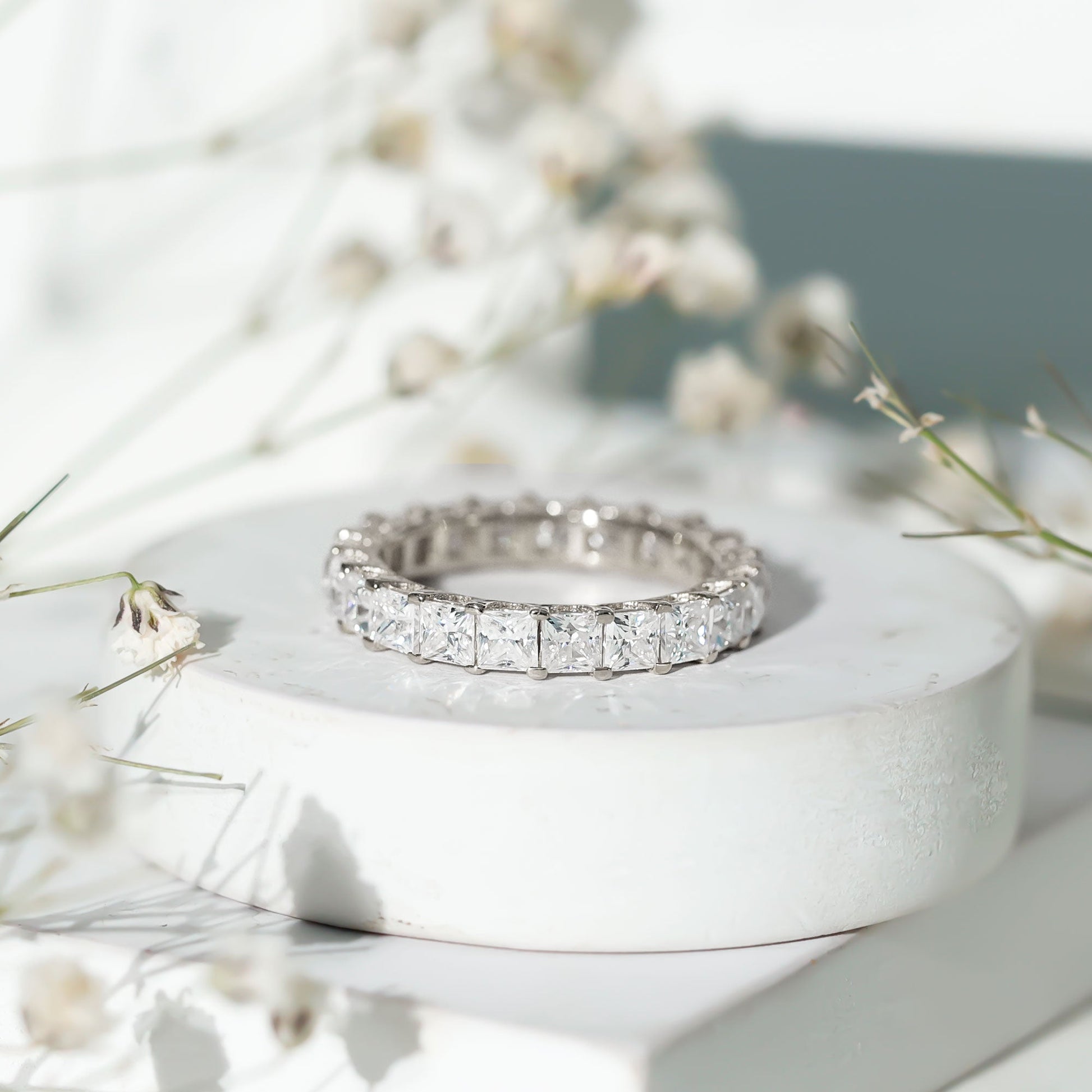 Silver ring with diamonds on a white stone surface with flowers in the background